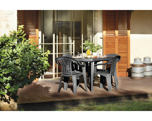 Gartenmöbel-Set aus Kunststoff mit ovalem Tisch und Armlehnstühlen auf einer sonnigen Holzterrasse vor dem Haus.