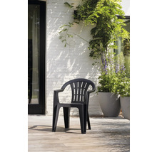 Stapelbarer Gartenstuhl aus schwarzem Kunststoff mit Armlehnen auf einer hellen Terrasse vor einer weißen Ziegelwand mit Pflanzen.