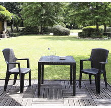 Zwei anthrazitfarbene Gartenstühle und ein quadratischer Tisch in Rattanoptik auf einer Holzterrasse vor einem grünen Garten mit Rasen und Bäumen.