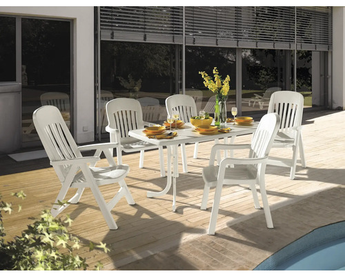 Gartenset bestehend aus einem weißen Esstisch aus Kunststoff und fünf weißen Gartenstühlen auf einer Holzterrasse neben einem Pool.