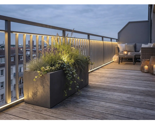 Beleuchtete Dachterrasse mit Holzdeck, Metallgeländer inklusive LED-Streifen, großem Pflanzkübel und Lounge-Möbeln bei Abenddämmerung.