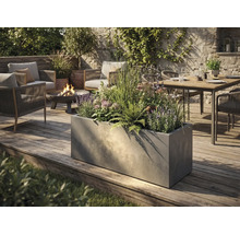 Großer rechteckiger Pflanzkübel in Betonoptik auf einer Holzterrasse in einem modern gestalteten Garten mit Sitzgruppe und Feuerschale.