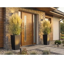 Moderner Hauseingang mit Holzhaustür, Steinverblendung und zwei hohen Pflanzkübeln in Rattan-Optik mit Pampasgras.