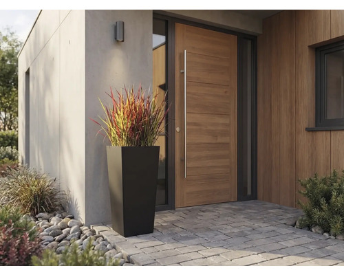 Hoher, quadratisch-konischer Pflanzkübel in Schwarz vor einer modernen Holzhaustür mit langem Griff und Pflastersteinen.