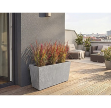 Rechteckiger grauer Pflanzkübel in Steinoptik mit Ziergras auf einer modernen Dachterrasse mit Holzboden und Loungemöbeln.