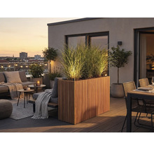 Moderner Dachbalkon mit beleuchtetem Holz-Pflanzkasten, hohen Gräsern, Loungemöbeln und Essbereich auf einer Holzterrasse bei Abenddämmerung.