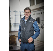 Mann trägt eine dunkelgraue Steppweste über einer blauen Fleecejacke und einer blauen Arbeitshose.