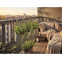 Balkon mit Kräutertöpfen am Geländer, Loungesofa mit Kissen und Decke, Holzfliesen, Laterne und Lichterkette vor einem Stadtpanorama.