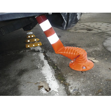 Flexibler Leitpfosten in Orange und Weiß, unter der Stoßstange eines Autos gebogen, daneben gelbe Fahrbahntrenner mit Reflektoren.