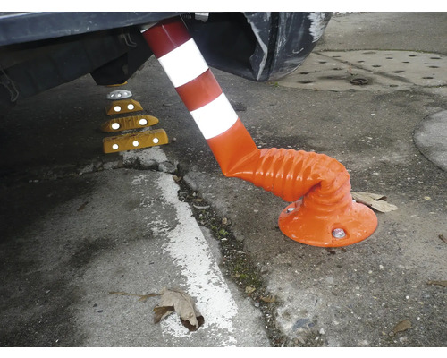 Flexibler Leitpfosten in Orange und Weiß, unter der Stoßstange eines Autos gebogen, daneben gelbe Fahrbahntrenner mit Reflektoren.