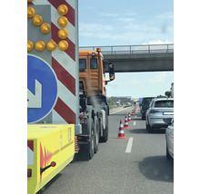 Baustellenabsicherung auf der Autobahn mit Absperrwagen, orangefarbenem Lastkraftwagen und Leitkegeln zur Verkehrsführung unter einer Brücke.