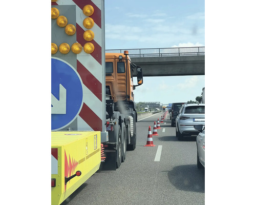 Baustellenabsicherung auf der Autobahn mit Absperrwagen, orangefarbenem Lastkraftwagen und Leitkegeln zur Verkehrsführung unter einer Brücke.