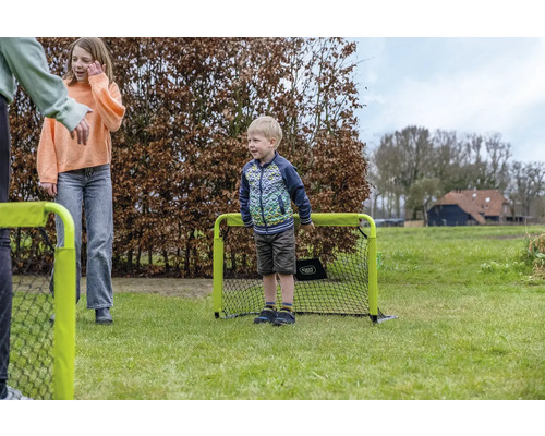 Kinder spielen mit einem kleinen tragbaren Fußballtor auf einer Rasenfläche im Garten.