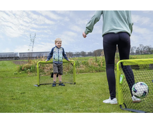 Kind und Erwachsener spielen Fußball im Garten mit zwei kleinen grünen Fußballtoren auf einer Rasenfläche.