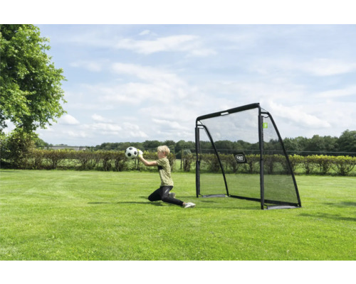 Ein Kind fängt einen Fußball vor einem schwarzen Fußballtor auf einem grünen Rasen in einem hellen, sonnigen Garten.