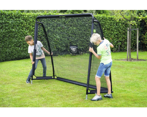 Zwei Jungen spielen im Garten mit einer EXIT Toys Rückprallwand auf einer Rasenfläche vor einer Hecke.