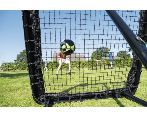 Fußball Rebounder Netz im Garten mit einem fliegenden Fußball und spielenden Personen auf einer Rasenfläche.