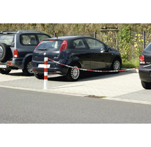 Organisierte Parkplatzszene im Freien mit einem rot und weiß gestreiften Absperrpfosten und Kunststoffkette neben geparkten Autos auf Pflastersteinen.