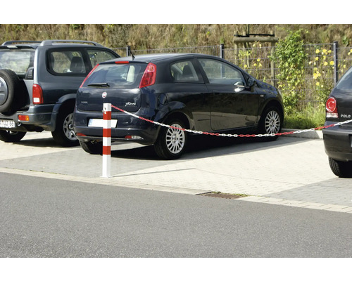 Organisierte Parkplatzszene im Freien mit einem rot und weiß gestreiften Absperrpfosten und Kunststoffkette neben geparkten Autos auf Pflastersteinen.