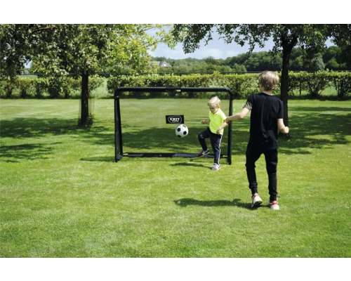 Zwei Kinder spielen Fußball mit einem EXIT Toys Fußballtor auf einer Rasenfläche in einem hellen, sonnigen Garten.