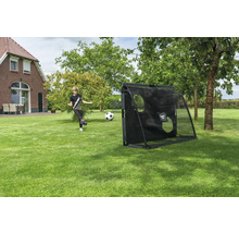 Ein Junge schießt einen Fußball auf ein schwarzes Fußballtor mit EXIT TOYS Logo und Torwandplane in einem großen Garten mit Rasen und Bäumen.