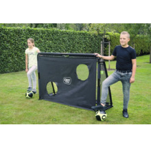 Zwei Kinder stehen mit Fußbällen neben einem schwarzen EXIT Toys Fußballtor mit Trainingswand inklusive zwei Ziellöchern auf einer Rasenfläche.