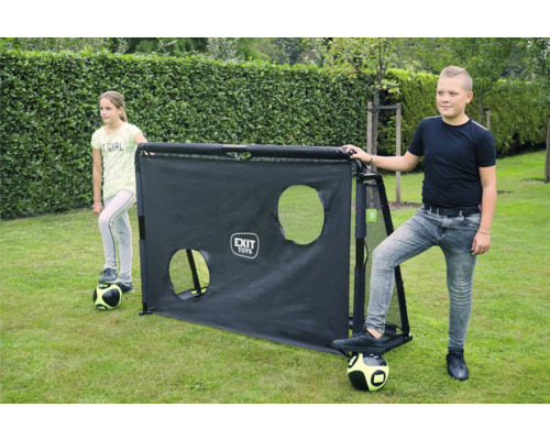 Zwei Kinder stehen mit Fußbällen neben einem schwarzen EXIT Toys Fußballtor mit Trainingswand inklusive zwei Ziellöchern auf einer Rasenfläche.