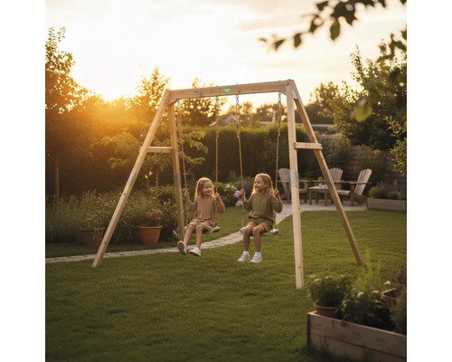 EXIT Toys Doppelschaukel aus Holz im Garten mit zwei spielenden Kindern bei Sonnenuntergang.