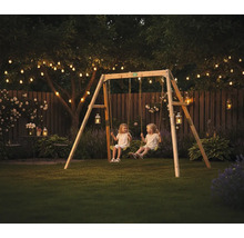 Holzschaukel Set in einem Garten am Abend mit Lichterketten und zwei Kindern auf den Schaukeln.