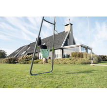 Spielgerät aus Metall im Garten mit Turnreck, Gymnastikringen und Schaukel, Kind turnt kopfüber an der Stange vor einem Haus mit Rasenfläche.