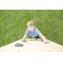Ein Kind klettert an einer Kletterwand aus Holz mit bunten Klettersteinen auf einer Rasenfläche.