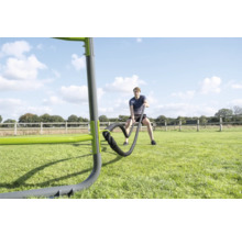 Ein Mann trainiert mit Battle Ropes an einer Outdoor Fitnessstation auf einer Rasenfläche in einem hellen, weitläufigen Außenbereich.