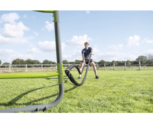 Ein Mann trainiert mit Battle Ropes an einer Outdoor Fitnessstation auf einer Rasenfläche in einem hellen, weitläufigen Außenbereich.
