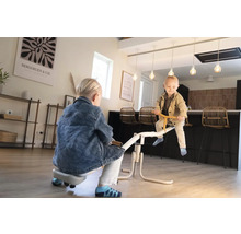 Zwei Kinder spielen auf einer weißen Wippe in einer modernen, hellen Wohnküche mit Holzboden.