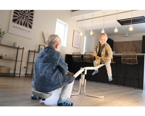 Zwei Kinder spielen auf einer weißen Wippe in einer modernen, hellen Wohnküche mit Holzboden.