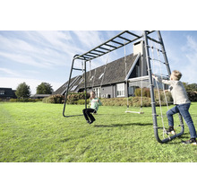 Kinder spielen auf einem großen Klettergerüst aus Metall im Garten mit Schaukel, Turnringen, Kletternetz und Hangelstange.