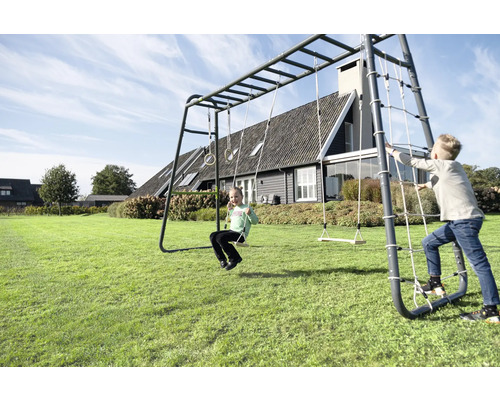 Kinder spielen auf einem großen Klettergerüst aus Metall im Garten mit Schaukel, Turnringen, Kletternetz und Hangelstange.
