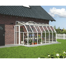 Helles, weißes Anlehn-Gewächshaus aus Aluminium und Glas an einer Ziegelwand mit Dachfenster und organisierten Pflanzen in einem Garten.