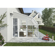 Moderner Anlehn-Wintergarten aus weißem Aluminium und Glas, an eine Hauswand montiert, auf einer gepflasterten Terrasse mit Gartenmöbeln.