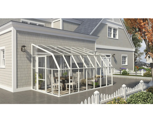 Weißer Anlehn-Wintergarten aus Aluminium und Glas an einem grauen Haus. Innenraum mit Holzmöbeln und Sofa auf einer gefliesten Terrasse.