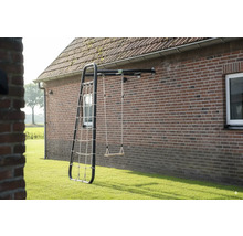 Wandmontiertes Spielgerät mit schwarzem Metallrahmen, einer Holzschaukel und einem Kletternetz an einer Ziegelwand im Garten.