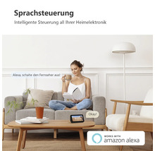 Intelligente Sprachsteuerung im Wohnzimmer mit einem Smart Display auf einem Holztisch neben einer Frau auf dem Sofa. Amazon Alexa Logo.