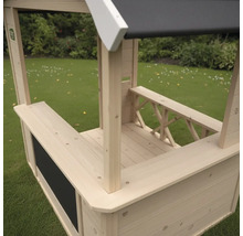 Spielhaus aus Holz in Kiosk-Optik mit Verkaufstresen und Kreidetafel auf einer Rasenfläche.
