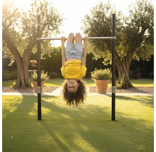 Kind hängt kopfüber an einer Reckstange aus Metall in einem weitläufigen Garten auf einer Rasenfläche.