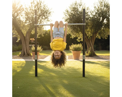 Kind hängt kopfüber an einer Reckstange aus Metall in einem weitläufigen Garten auf einer Rasenfläche.