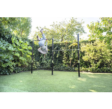 Doppel-Reckstange aus Metall im Garten, ein Kind turnt kopfüber an der Stange, umgeben von Hecken und Rasen, helle und weitläufige Atmosphäre.
