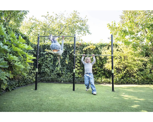 Zwei Kinder spielen an einer Doppel-Reckstange aus Metall im Garten auf einer Rasenfläche.