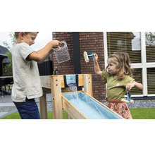 Zwei Kinder spielen an einer Wasserbahn aus Holz im Garten. Ein Junge gießt Wasser aus einem Krug, ein Mädchen spielt mit kleinen Holzbooten.