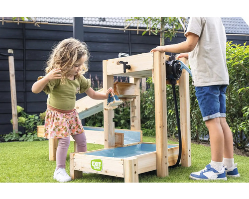 Kinder spielen im Garten mit einer EXIT Toys Wasserbahn aus Holz, ausgestattet mit einer Wasserpumpe und mehreren Ebenen auf grünem Rasen.
