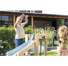 Kinder spielen im Garten mit einer hölzernen Wasserbahn. Ein Junge gießt Wasser aus einem Messbecher in die obere Rinne.